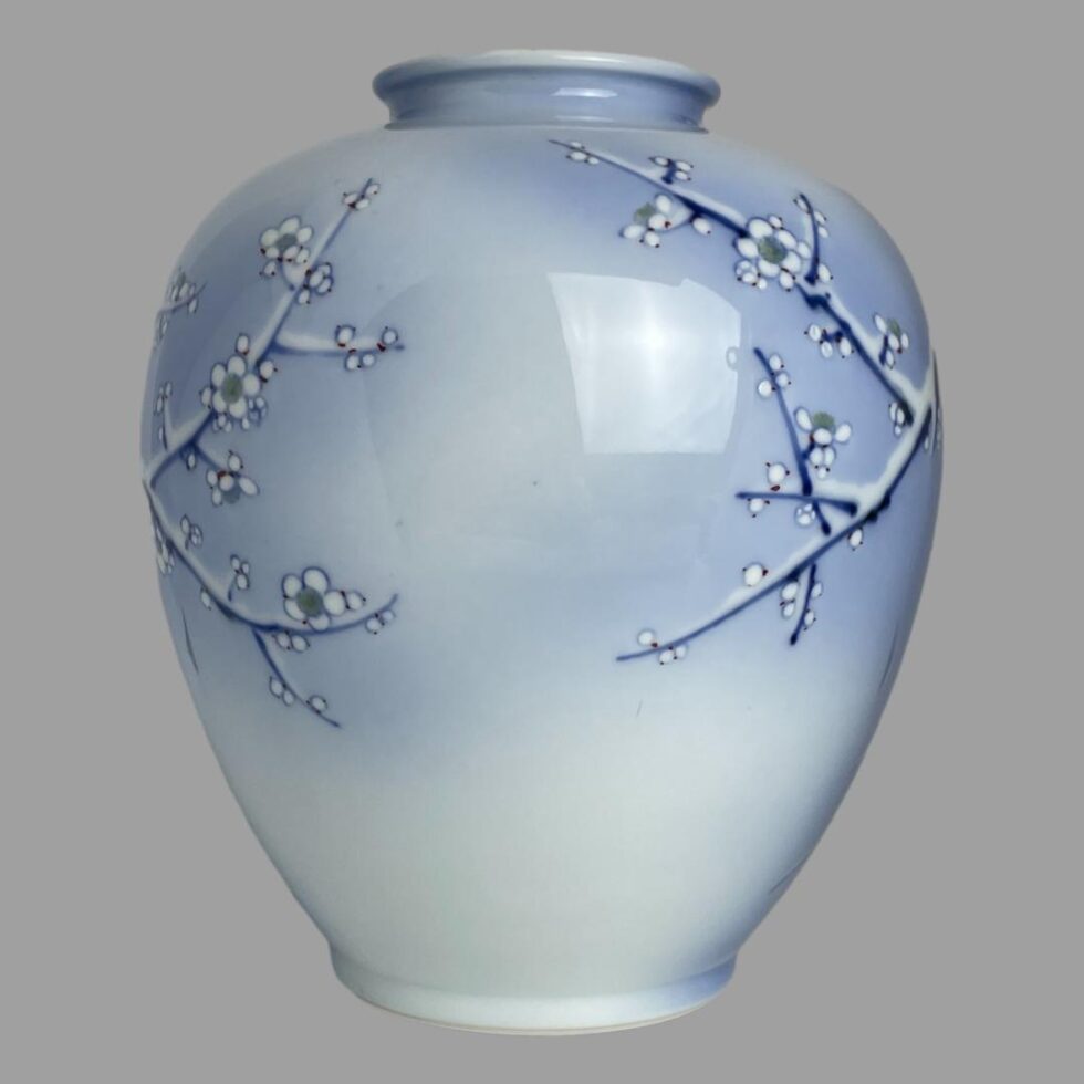 Photo of Fukagawa vase showing just branches of flowering white winter plum protruding from the left and from the right with a bare centre area. Appears as though the branches are reaching out to toucher each other.