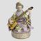 Main photo of Dresden geisha with shamisen displayed with the geisha forward facing. She is sitting in seiza position (on her knees with buttocks on heels) Her kimono is very colourful and not traditional Japanese pale green and white striped under kimono covered with a yellow kimono with red white and blue flowers and green foliage and pale pink outer areas (collar, sleeves etc) Her obi(belt sash) has vertical green cerise and white stripes at the top and a short area beneath with horizontal lines in same colours. She is a right handed player so the shamisen neck is held in her left hand with the body to the right and her right hand holding the bachi (large plectrum)