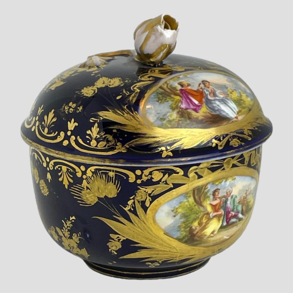 Photo of the small Meissen lidded pot this time with the images turned to the right a little showing the contrast of the hand-painted romantic 'windows' and the dark royal blue and gilt areas.
