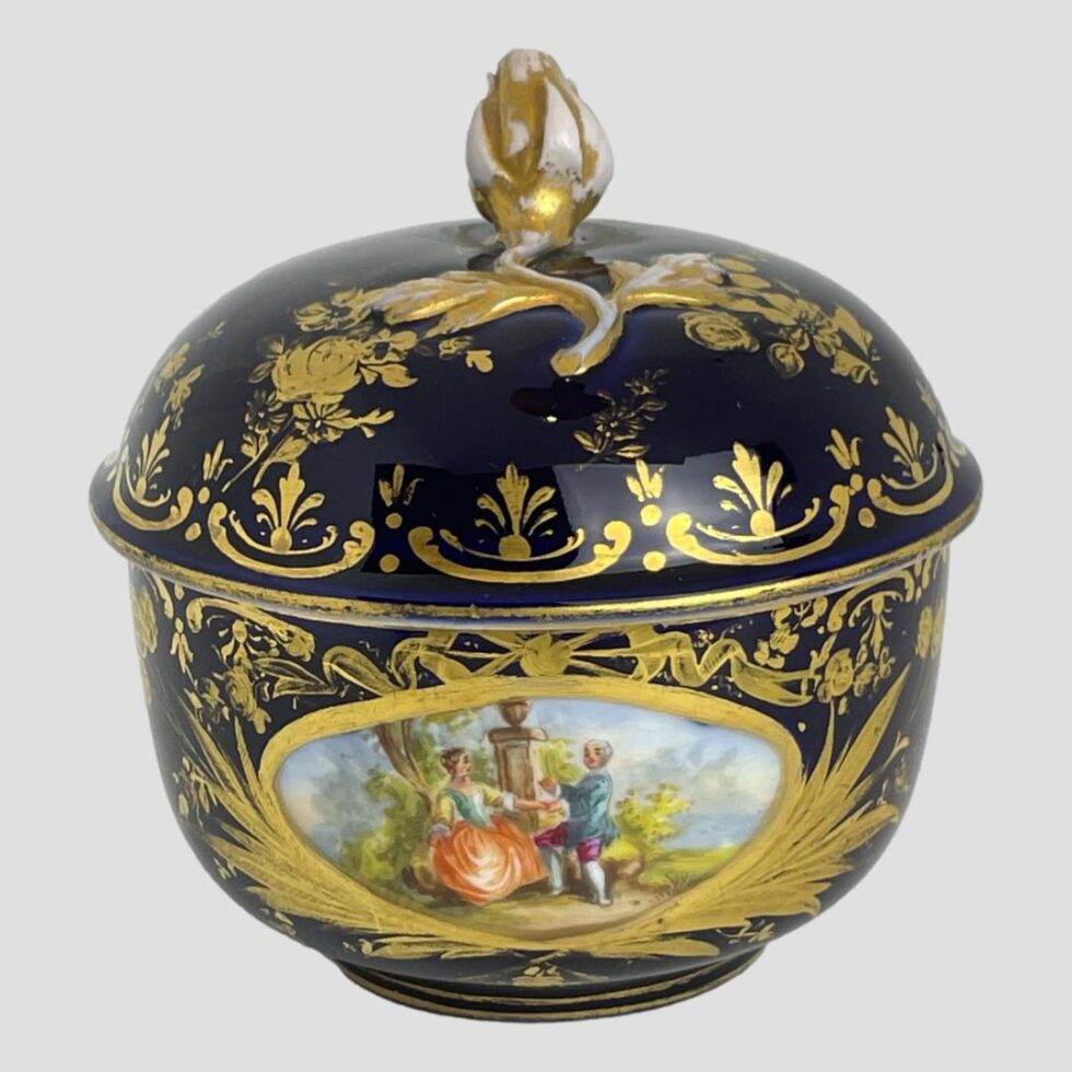 Photo of the other romantic image 'window' on the bottom part of the pot. This time, a courting couple are seen again, in brightly coloured Georgian attire, by a garden plinth with an urn on top. The man is holding the ladies left hand and appears possibly? to be holding something between his fingers. Could it be a ring?