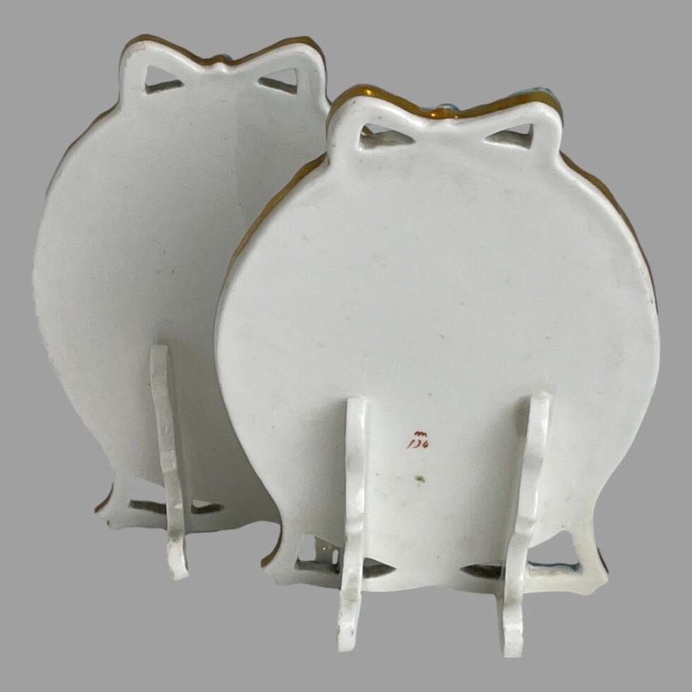 Photo of the backs of both Minton porcelain pictures with the one with red stamp in the foreground to the right and other behind and to the left/