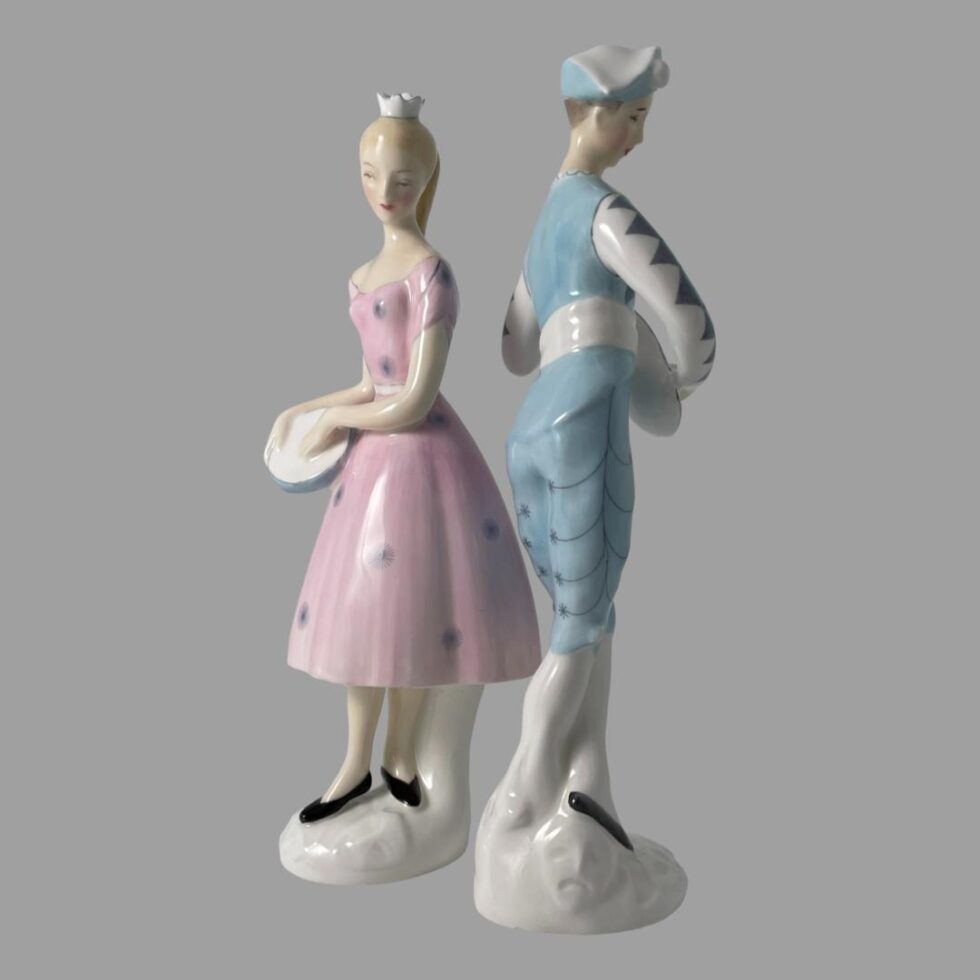 Photo of Doulton figurines displayed almost back to back. Columbine is on the left with her left side on display while Harlequin is displaying his right side. Columbine's face is turned to camera whilst Harlequin faces more to the right.