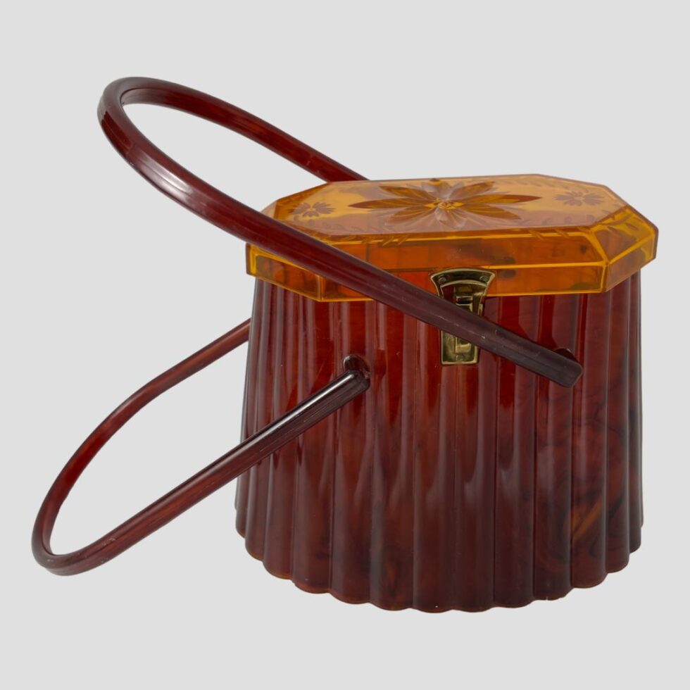 Photo of 50s moulded acetate purse this time with both handles leaning over to the left. The righthand handle stops just above the left side of bag and the lefthand handle is touching the surface on the left.