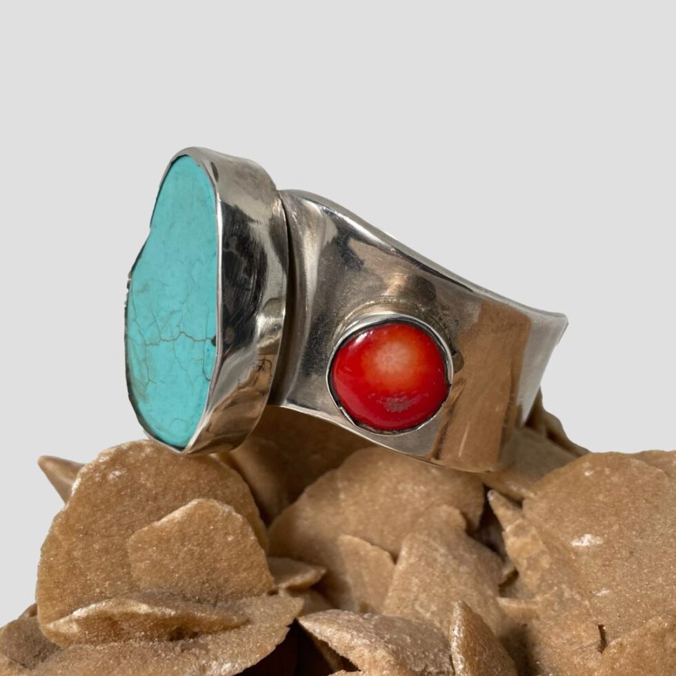 Photo of the Mexican wavy cuff still on top of a rock of natural desert rose this time with the front facing left showing one coral area in full and the turquoise to its left facing left.