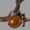Main photo of Deco style amber brooch displayed leaning against a small twig of cherry tree. The amber cabochon has some inclusions that look like the dots on a ladybirds back and the brooch pin, which is visible through the amber gives an impression of the split of the ladybirds wings. The silver cala lily flower heads are to one side, in this photo to the top right with one above the other so creating a half frame of flowers and the flower stems hug the lower frame of the amber (in this photo)