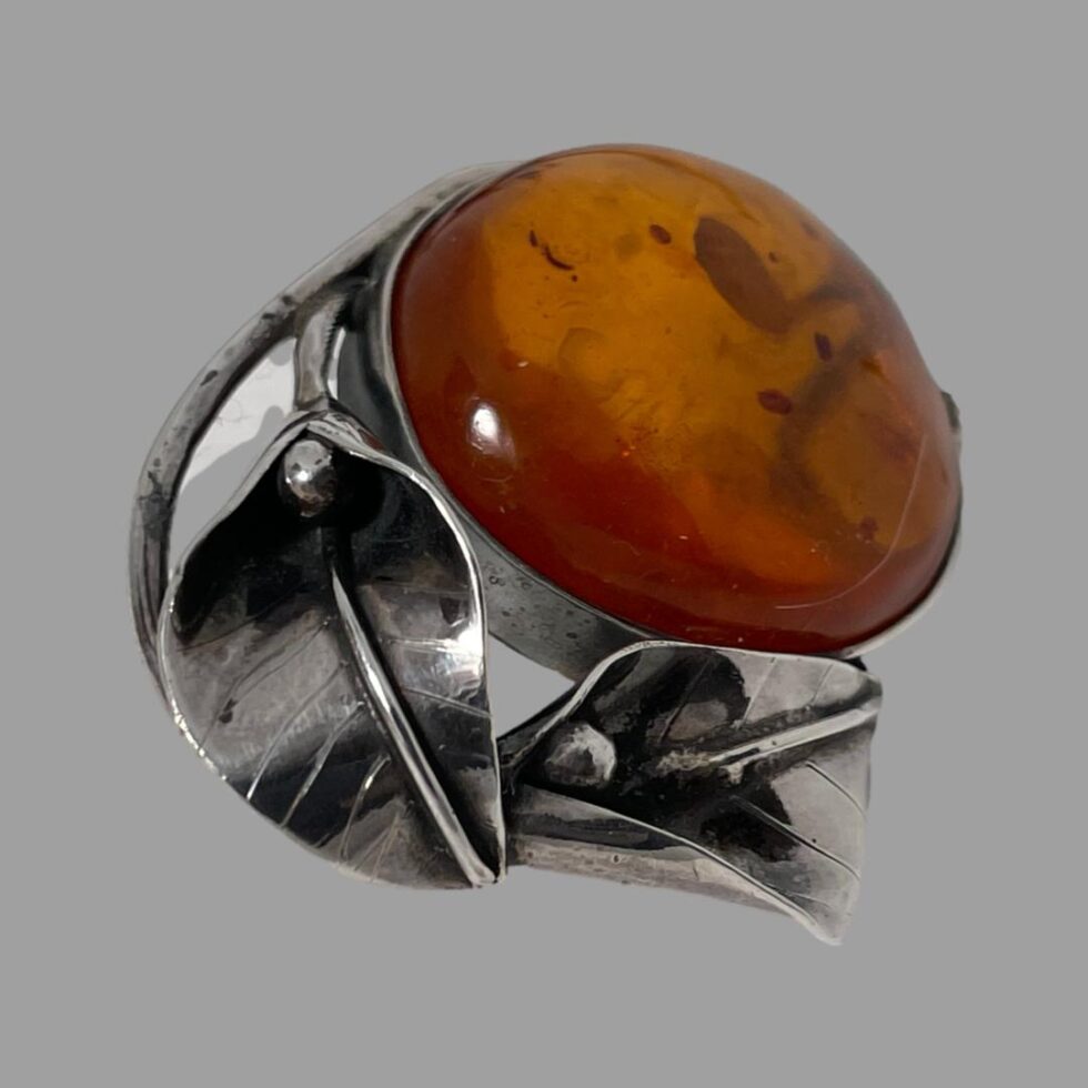 Photo of the amber Deco style brooch seen from a side angle with the amber facing towards the upper right and the cala lily flower heads upside down on the bottom left.