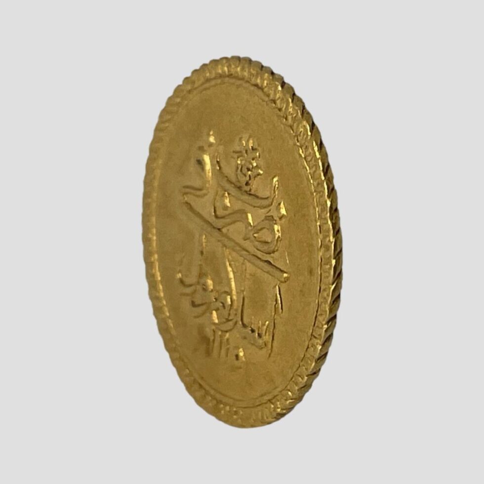 Photo of the gold Ottoman coin displayed at a slight side angle showing the outer edge. The reverse side of the coin is visible to the left..
