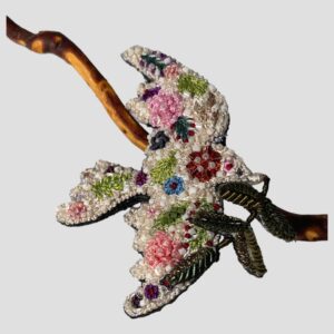 Main photo of trovelore peace dove brooch displayed leaning against a twig of cherry in the background with the dove flying to the right. The beadwork and the embroidery of this piece is exquisite. The dove is a creamy white base colour with embroidered flowers and leaves embellished with different colour bead. It is a thing to bring much joy on beholding. Lovely gift for someone special or yourself!