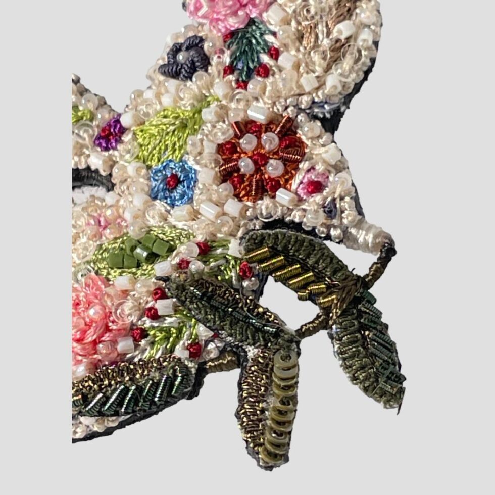 A close up photo of the doves head with olive branch in its beak highlighting the incredible embroidery and beadword.