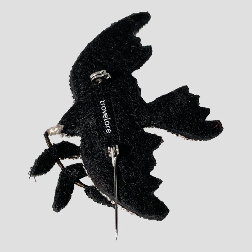 Photo of the back of the peace dove brooch which has a black felt like backing with a label in the centre for Trovelore.