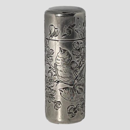 Main photo of c1888 silver scent bottle seen from an eye level with the opening front side in the foreground. The engraved decoration on this side shows 2 birds perched on a branch of cherry in blossom. The bird in the background is looking up at a butterfly on the front of the lid and the other is looking towards the left. Very detailed fine engraving to birds, flora and butterfly. These scent bottles were most likely used by ladies or even gentlemen when travelling. It is nice and compact with the original glass stopper inside which closed tightly and the lid of course with good closure.