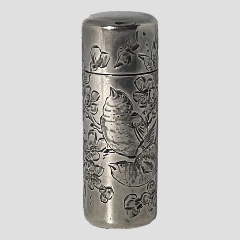 Main photo of c1888 silver scent bottle seen from an eye level with the opening front side in the foreground. The engraved decoration on this side shows 2 birds perched on a branch of cherry in blossom. The bird in the background is looking up at a butterfly on the front of the lid and the other is looking towards the left. Very detailed fine engraving to birds, flora and butterfly. These scent bottles were most likely used by ladies or even gentlemen when travelling. It is nice and compact with the original glass stopper inside which closed tightly and the lid of course with good closure.