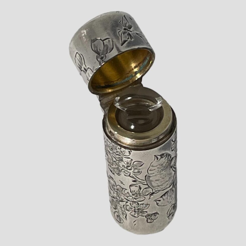 Photo looking diagonally downward at the antique silver scent bottle this time shown with the lid open and the glass stopper visible in place. The inside of the lid has gilt lining to protect the silver from the acidity of the scents.