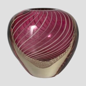 Main photo of Vicke Lindstand zebra vase seen from an eye level with one wide side on display. The shape of the vase is like a heart but without the little dip bit at the centre top. It has a narrower base in clear glass with some of the filigree strands looking like a fine net visible just below where the pink starts. The upper part balloons out into a bulbous finish with the vase opening sat in the middle at the top (not the whole of the top is open) The pink is a lovely shade and the white filigree swirls finish this piece perfectly.
