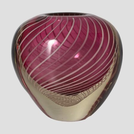 Main photo of Vicke Lindstand zebra vase seen from an eye level with one wide side on display. The shape of the vase is like a heart but without the little dip bit at the centre top. It has a narrower base in clear glass with some of the filigree strands looking like a fine net visible just below where the pink starts. The upper part balloons out into a bulbous finish with the vase opening sat in the middle at the top (not the whole of the top is open) The pink is a lovely shade and the white filigree swirls finish this piece perfectly.