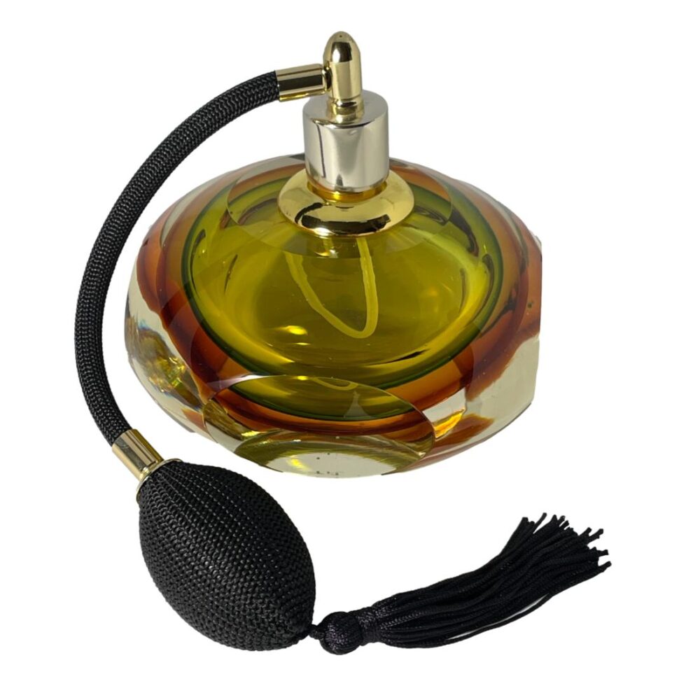 Photo looking at Murano perfume atomiser this time with one of the 4 flat sides in the centre foreground. The angle is more raised from main photo angle and the light is shining on the glass. The ball puff of the spray atomiser is now almost in the centre foreground with the tassels across the front.