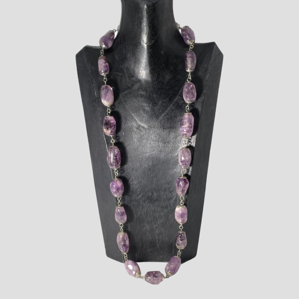 Photo of large amethyst beads necklace displayed on a black wooden display stand and shown forward facing. We use this stand for longer necklaces but even this one is unable to accommodate this substantial necklace! (Actually only 3 of the beads are on the flat surface in front of the stand.)