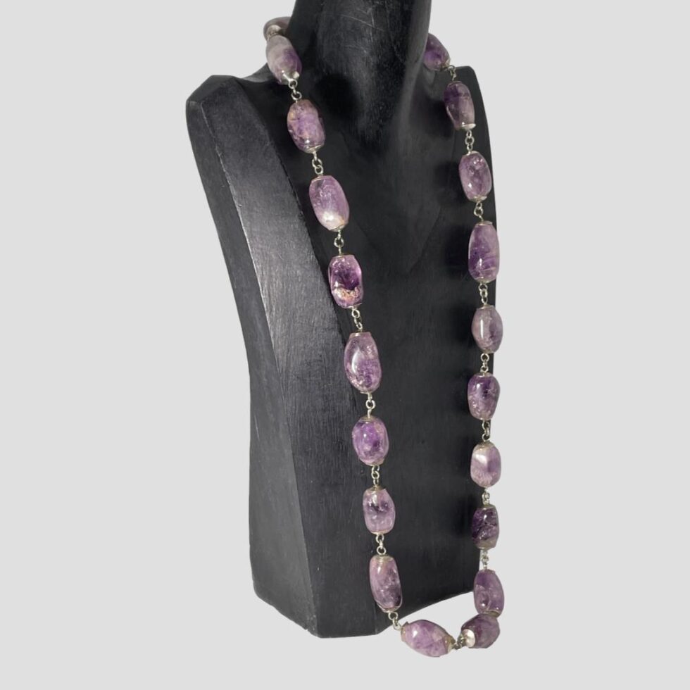 Photo of the large amethyst bead necklace still displayed on the black wooden stand this time with the necklace front facing right.