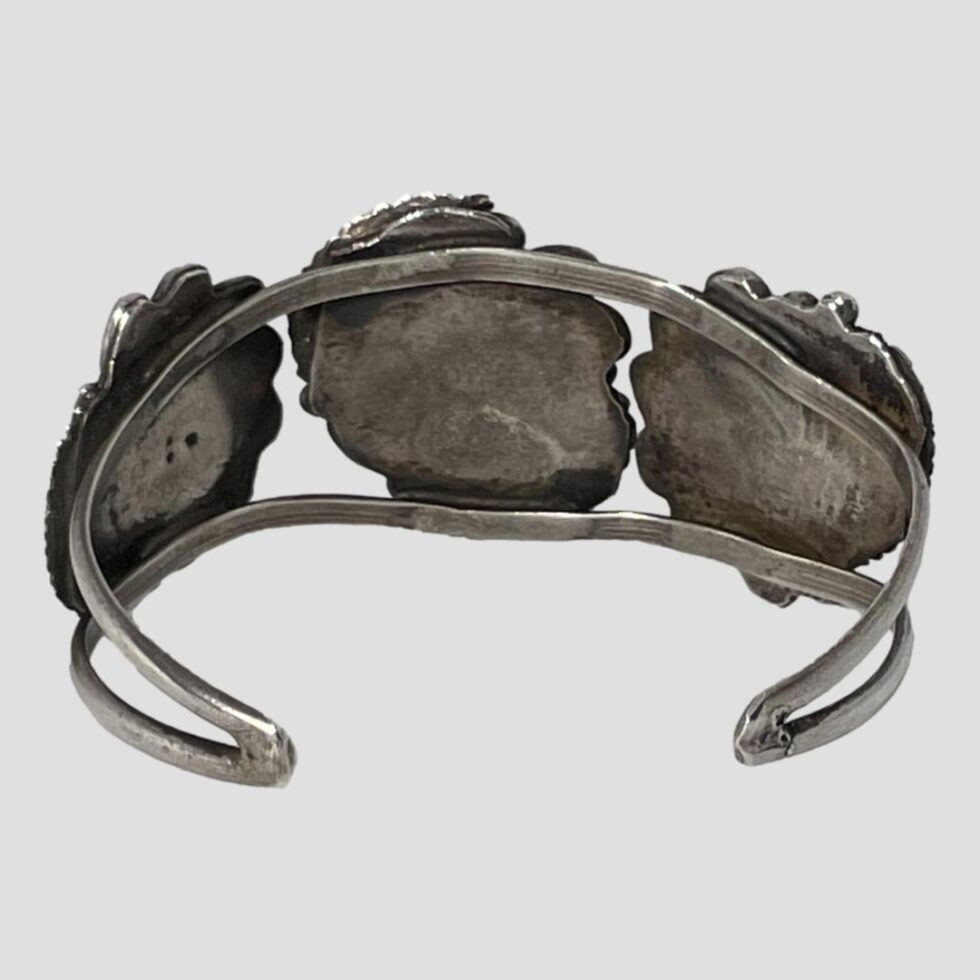Photo of the back of the cuff bracelet showing the backs of the discs that the turquoise are set on. The bracelet part itself is silver but unmarked and consists of 2 flat bands that join at the ends in a smooth curve.