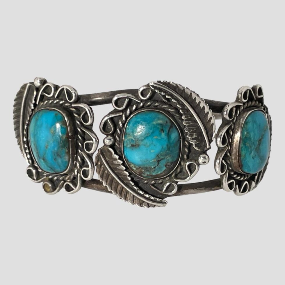 Photo of Navajo turquoise cuff bracelet displayed on a flat surface with the bracelet front forward facing. Although the discs the turquoise is set on is not silver, the turquoise stones themselves are of very high quality and are a deep shade of turquoise blue with dark inclusions.