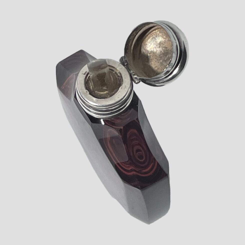 Photo looking down diagonally at the top of the scent bottle. The bottle opening front is facing to the bottom leeft corner and the lid is shown open with the glass stopper in place.