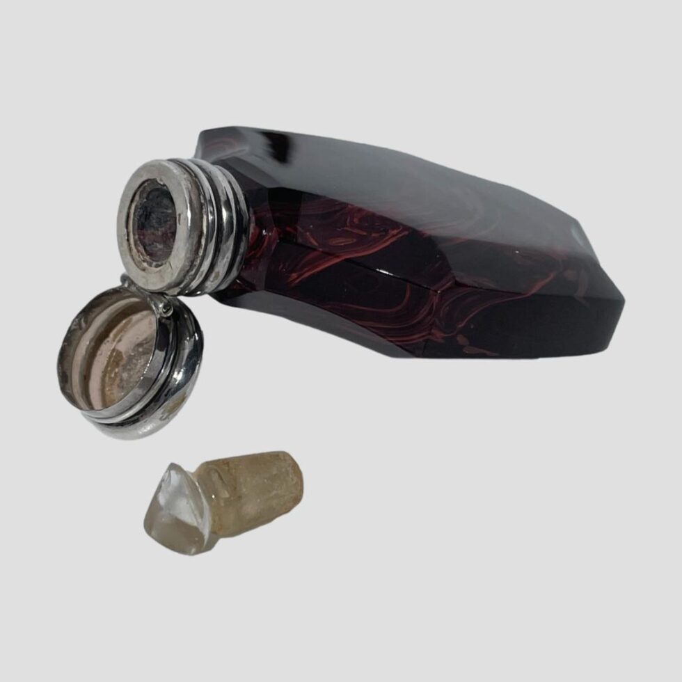 Photo of antique French scent bottle displayed open, reclining with the bottle opening raised up by the open lid and the glass stopper removed and placed in the foreground.
