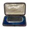 Main photo of antique tourmaline specimen brooch displayed inside its fitted case. The brooch is a wide oblong shape bordering on rectangular. The tourmaline is a grey/black colour and in a natural crystalline form and not polished smooth. The silver frame around the tourmaline is relatively thin in comparison but nicely executed with a plain flat silver frame around the edge of the tourmaline followed by a twisted silver band and finally set on a smooth round edged silver main frame. This brooch is all about the tourmaline! Black tourmaline is renowned for grounding the mind, relieving stress and shielding from negativity. Owing to its size and weight, this brooch would ideally suit a heavy overcoat or jacket.