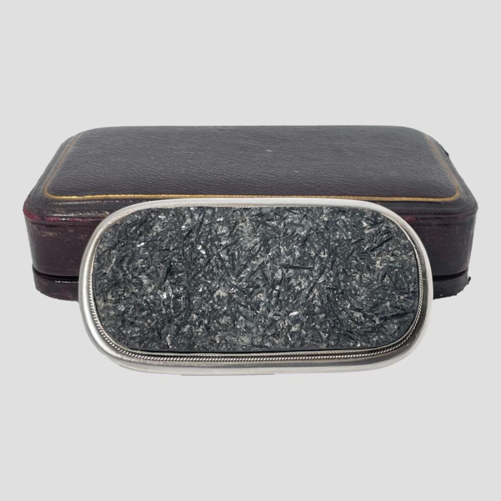 Photo of large tourmaline brooch again propped up in front of its case which is now shown closed. There is little wear to the top of the case and a little wear just visible to the bottom on the right.