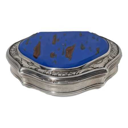 Main photo of William Lestourgeon silver box looking diagonally down from above to show the aventurine glass top. The main colour of the glass is a rich blue with small patches of copper coloured glittery specks. The silver around the aventurine glass has fine floral engravings all around whilst the rest of the box is in plain silver. Aventurine glass can feel like plastic as it is a man-made material very not to be mistaken for the crystal aventurine.