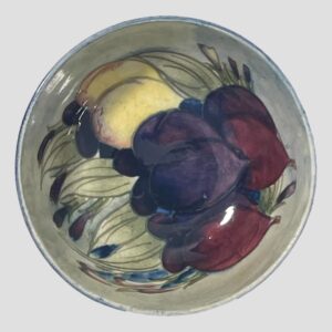 Main photo of Moorcroft wisteria footed bowl showing the stylised images of wisteria which appear like a type of plum fruit. These are in purple, mauve and yellow with wispy pale green leaves.