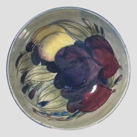 Main photo of Moorcroft wisteria footed bowl showing the stylised images of wisteria which appear like a type of plum fruit. These are in purple, mauve and yellow with wispy pale green leaves.
