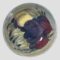 Main photo of Moorcroft wisteria footed bowl showing the stylised images of wisteria which appear like a type of plum fruit. These are in purple, mauve and yellow with wispy pale green leaves.