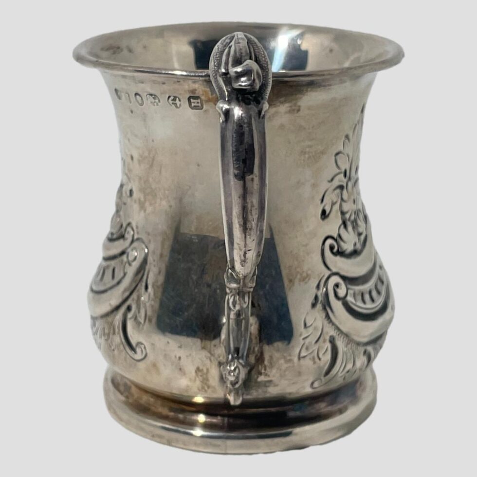 Photo of Victorian silver jug with the handle in the centre foreground. The hallmark is visible to the top left just below cup rim. The design pattern on both sides of the cup is the same.