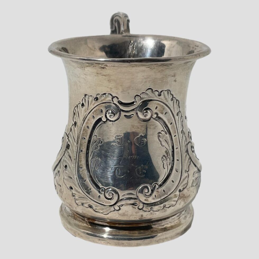 Photo of the engraved cartouche area of the Victorian silver cup. There are scroll like frames to the left and right and the outer area is all foliage.