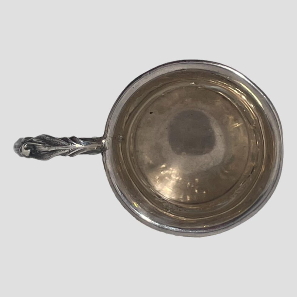 Photo looking straight down into the silver cup from above. The inside is fairly clean for an item of this age. The handle is to the left.