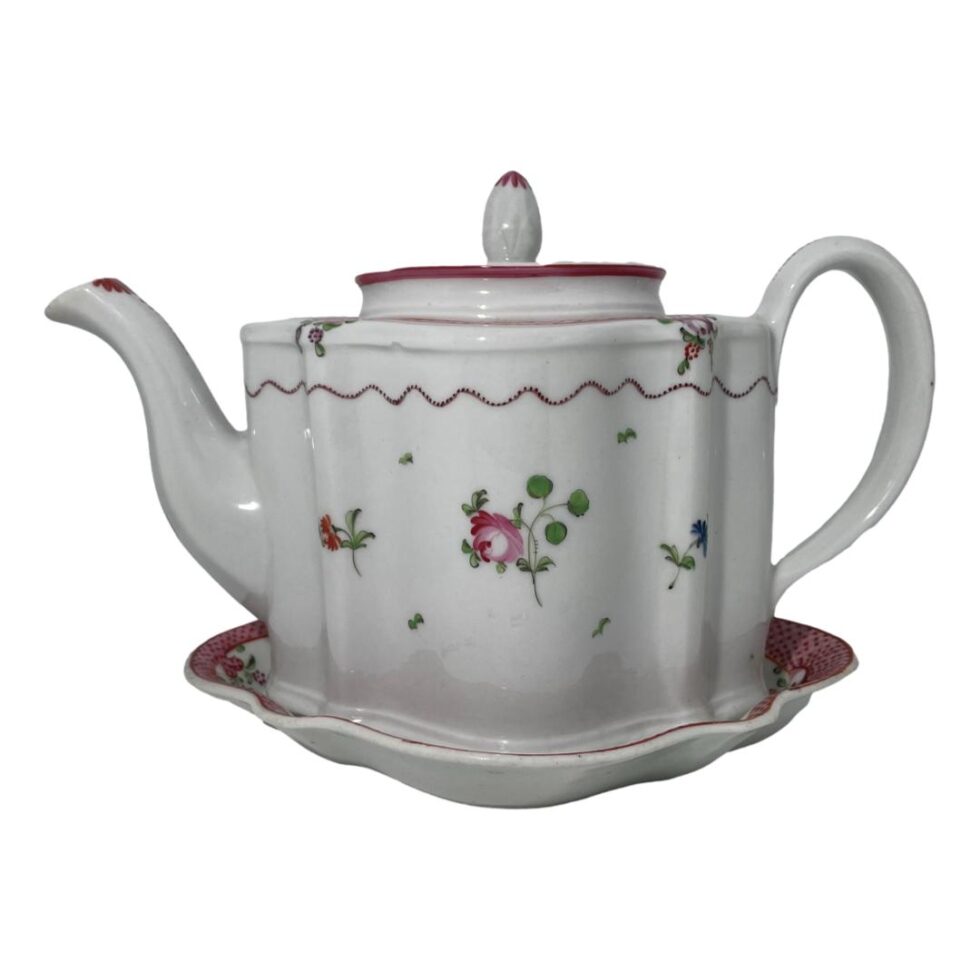 Photo of the teapot on its stand seen from an eye level. The teapot appears top heavy for the stand which is considerably smaller but it fits the pot like a glove! The spout is to the left.