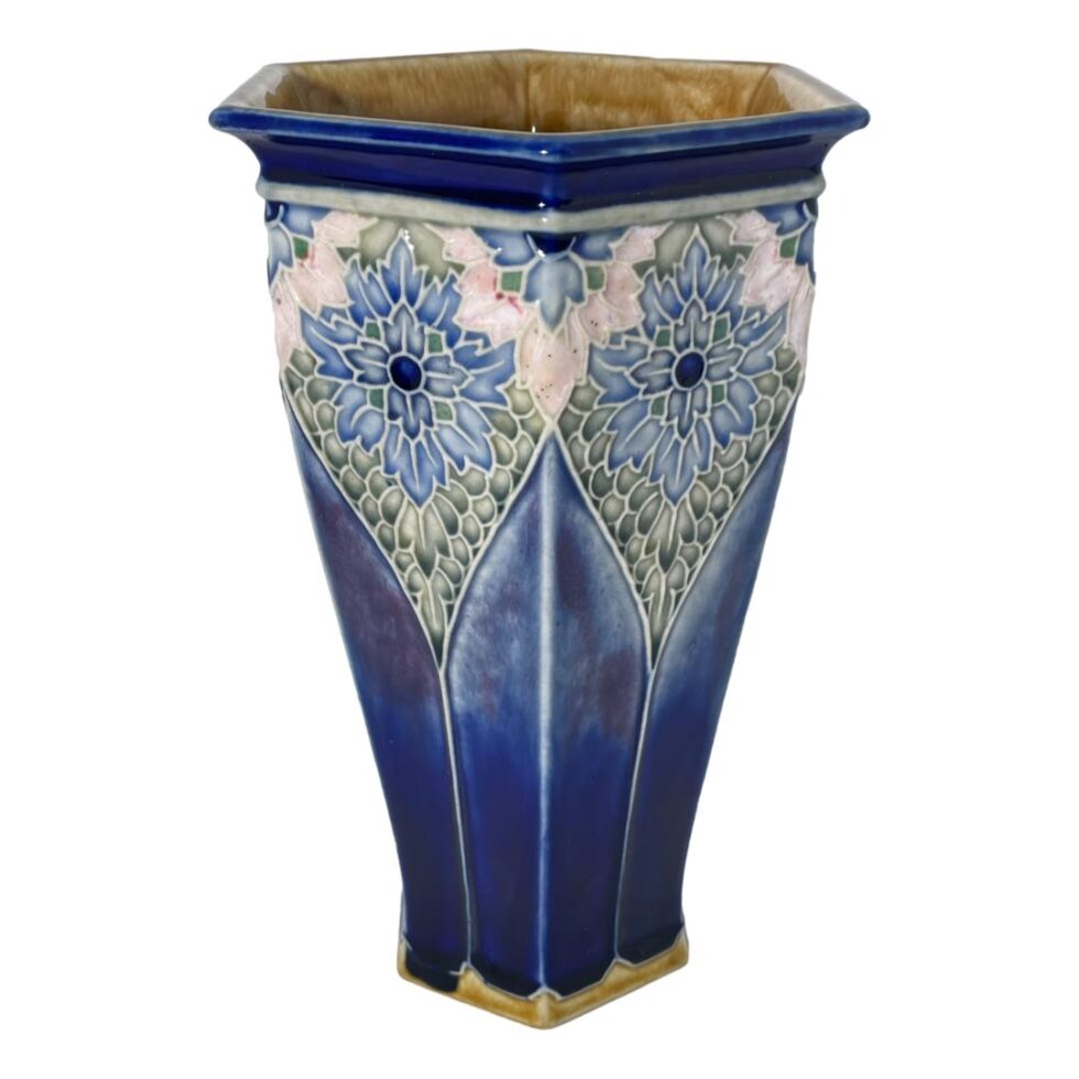 Photo of hexagonal Royal Doulton vase seen this time with one of the edges in the centre foreground and 2 sides of the hexagon either side. At the bottom on extreme left, you can see what appears to be a possible blue glaze run which covers the mustard yellow glaze for that segment. If you look on the exact opposite side however, this same phenomenon occurs in exactly the same place!