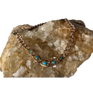 Main photo of Victorian gold turquoise bracelet displayed on a rock of natural river quartz. The clasp is closed and the the bracelet is laid in a circle on the rock. At the front of the rock are the 5 graduating turquoise set chain links with the largest turquoise at the centre. The stones are oval shaped to compliment the links of the chain which are also graduating. The rose gold and turquoise stone colour pairing is perfectly matched.