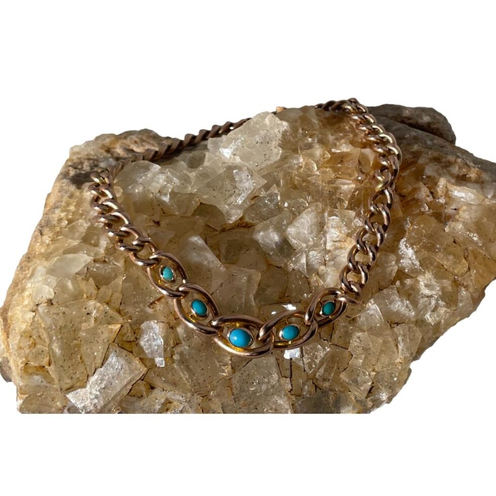 Main photo of Victorian gold turquoise bracelet displayed on a rock of natural river quartz. The clasp is closed and the the bracelet is laid in a circle on the rock. At the front of the rock are the 5 graduating turquoise set chain links with the largest turquoise at the centre. The stones are oval shaped to compliment the links of the chain which are also graduating. The rose gold and turquoise stone colour pairing is perfectly matched.