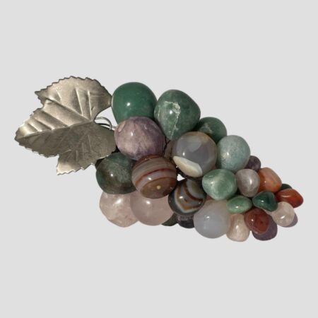 Main photo of vintage semi-precious stone grapes shown laid horizontally across the page with the top of the bunch on the left. The grapes are made of different semi-precious stones including amethyst, rose quartz, aventurine, agate and more. Colours range from greens to purples, pinks and reds. There is a silver tone metal leaf and tendrils. Lovely decorative item making a great addition to faux fruit bowl.