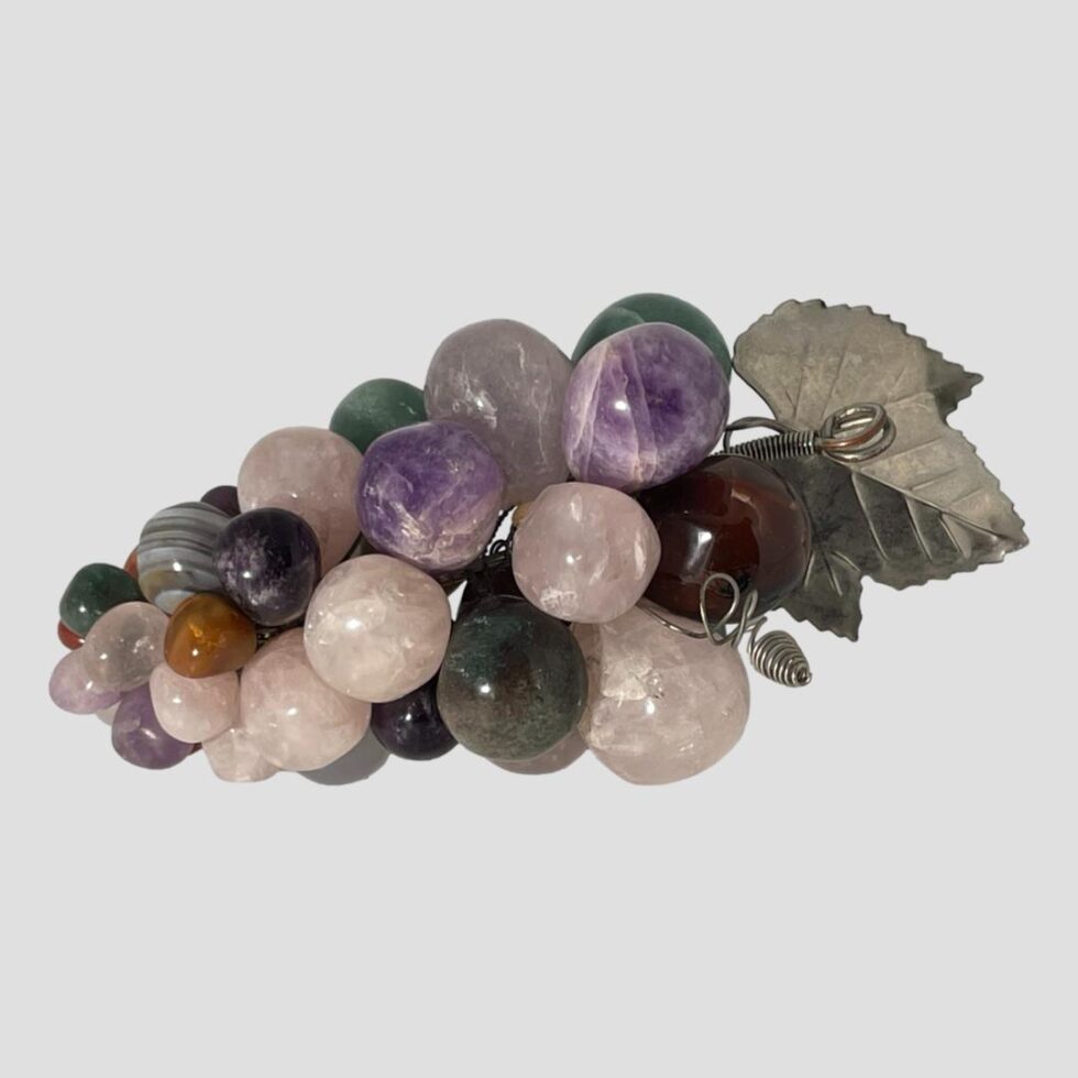 Photo of the bunch seen with the lower side on display this side has the most rose quartz and amethyst grapes. The curly metal tendrils are visible behind the leaf.