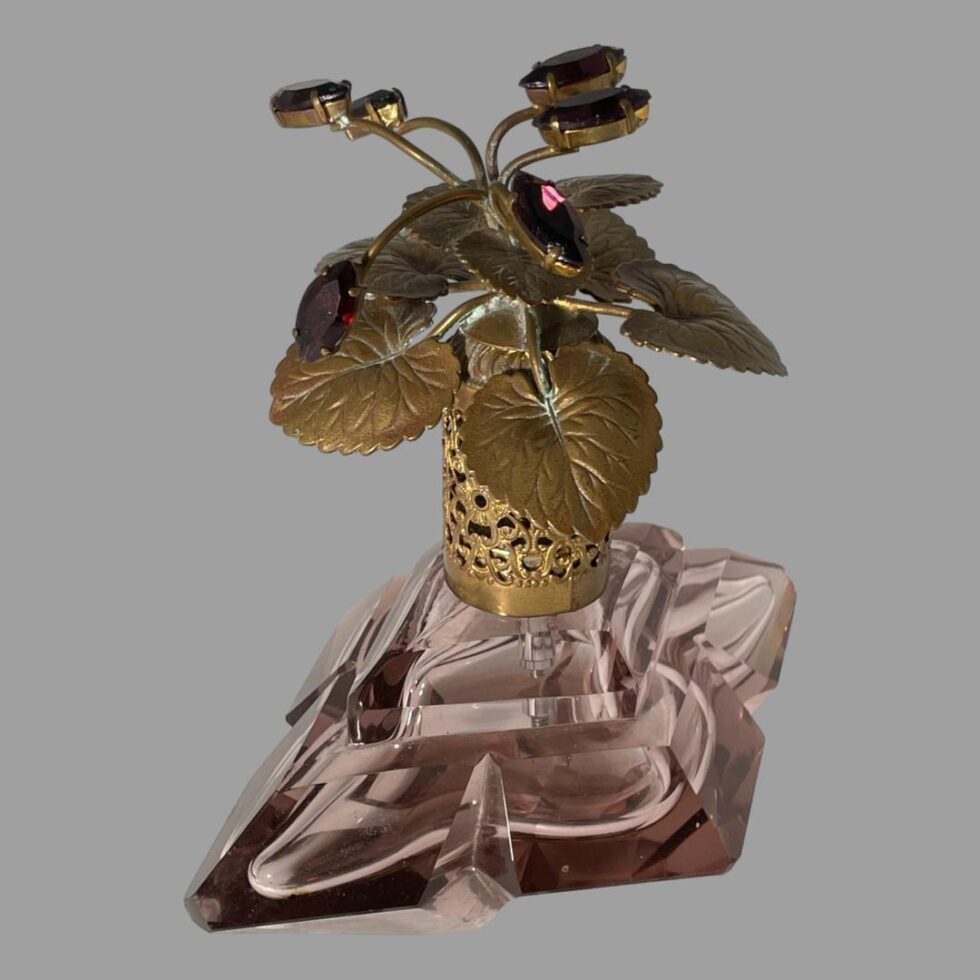 Photo of Irice scent bottle turned slightly so the wider side is along the bottom right corner of picture. The angle is a little raised and looking diagonally downward to show a good deal of the lid, the filigree area on the neck and most of the top of the diamond shaped bottle.