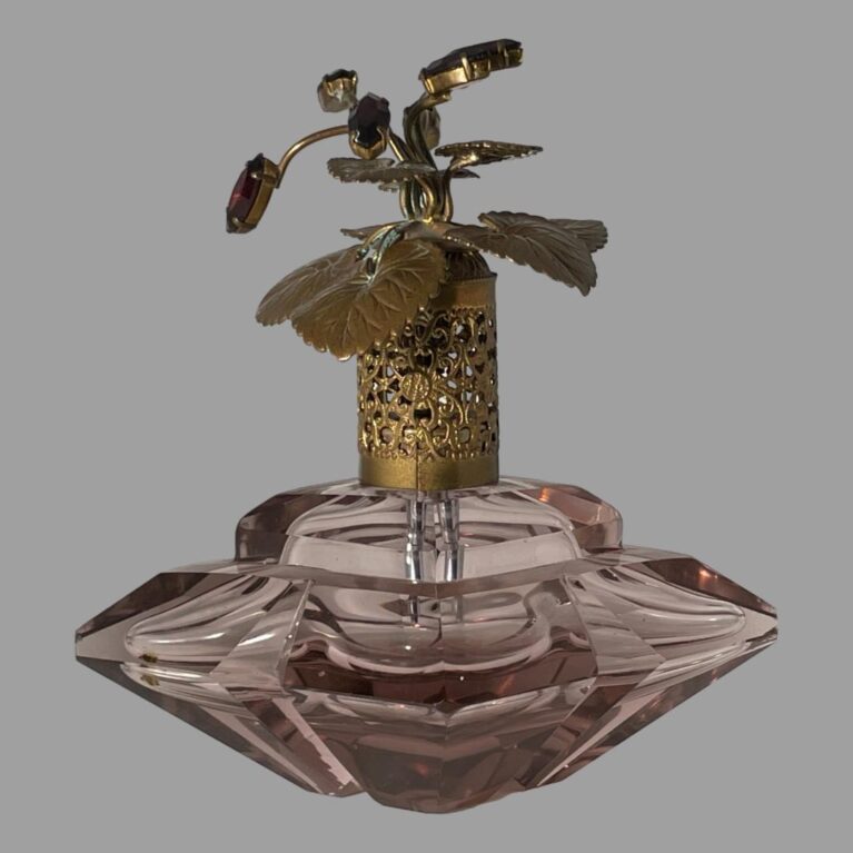 Main photo of vintage Irice scent bottle seen from an eye level with the wide side in the foreground. The filigree gilt metal neck of the lid is clearly visible and the structuring of the gilt metal leaves and stalks holding the purple rhinestones although the rhinestones themselves are not very visible here. The inner tube which attaches to the pump is absent but should be easy to replace. Even if not used for scent, this is a beautiful glass objet d'art!