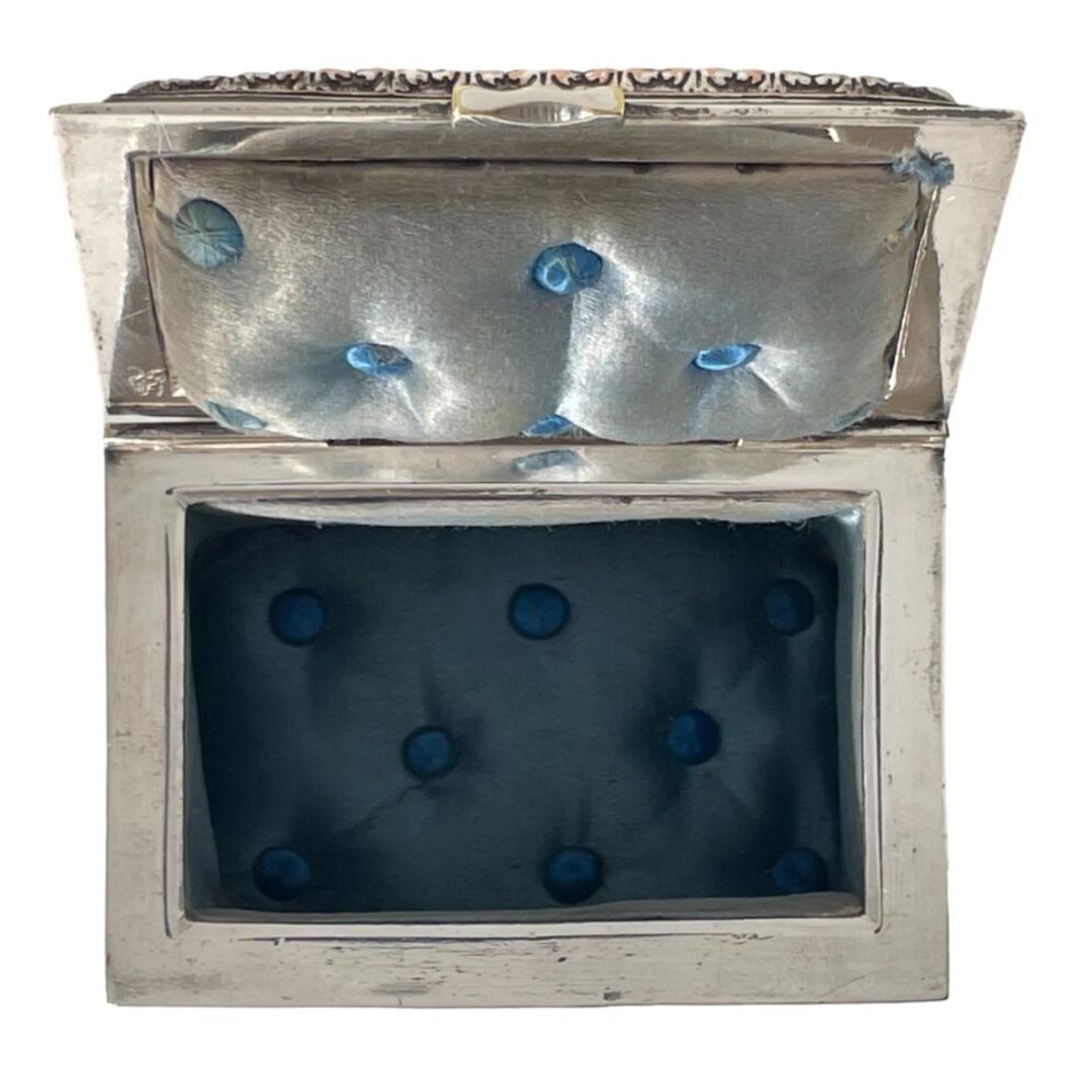 Photo of French repousse casket displayed this time with the lid open exposing the padded pale blue silk interior on the lid with turquoise blue buttons. The blue silk inside the casket is a little brighter in blue colour and also has turquoise coloured buttons. The single goats head stamp is just visible to the bottom left corner of the inside lid.