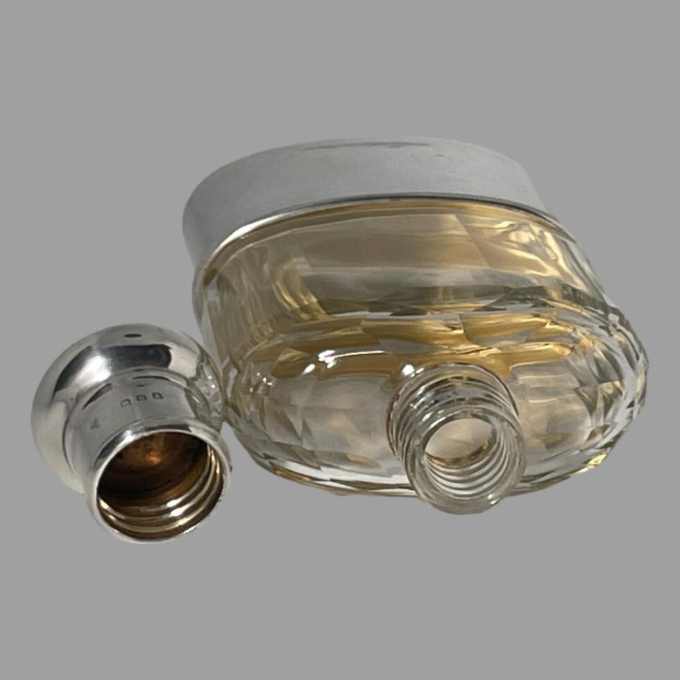 Photo of hip flask displayed laid flat with lid removed. The open mouth of the flask is to the right foreground and the inside of the lid is to the left. The gilt interior of the removable cup base is clearly visible at this angle.
