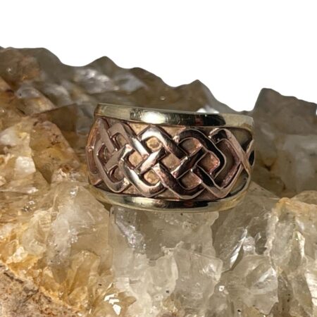 Main photo of Clogau Welsh gold ring displayed on top of a rock of natural river quartz with the ring front forward facing. There is a panel with a Celtic knot design in rose gold at the front which takes up about half of the ring with the remaining half in yellow gold. It is a good solid chunky ring in a smaller size perfect pinkie ring.