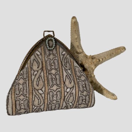 Main photo of 1930s Parisian beaded bag displayed upright with the beaded clasp side forward facing. There is part of a starfish behind the bag as the beading pattern on the bag has a sea urchin / coral like look about it. The bag is triangular in shape with a square edged brass hook right at the top where a handle probable was originally. The opening clasp is a sweet circle of small pale green beads. The beads of the bag are a pale orangey pink, with even paler pink and spelter beads with a couple of small pockets of white beads. A very special bag this!