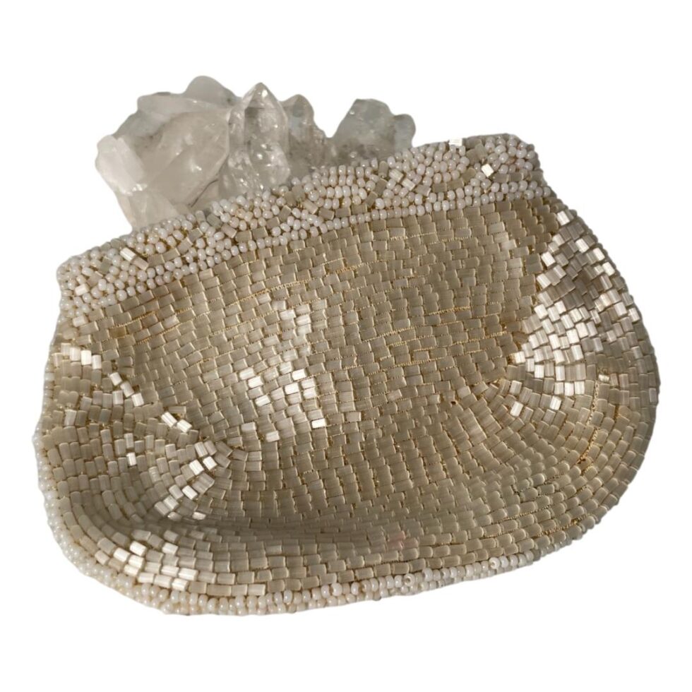 A photo of the back of the small purse which is covered in small white shimmering beads. The purse is leaning up against the rock of quartz crystal which can be seen in the background.