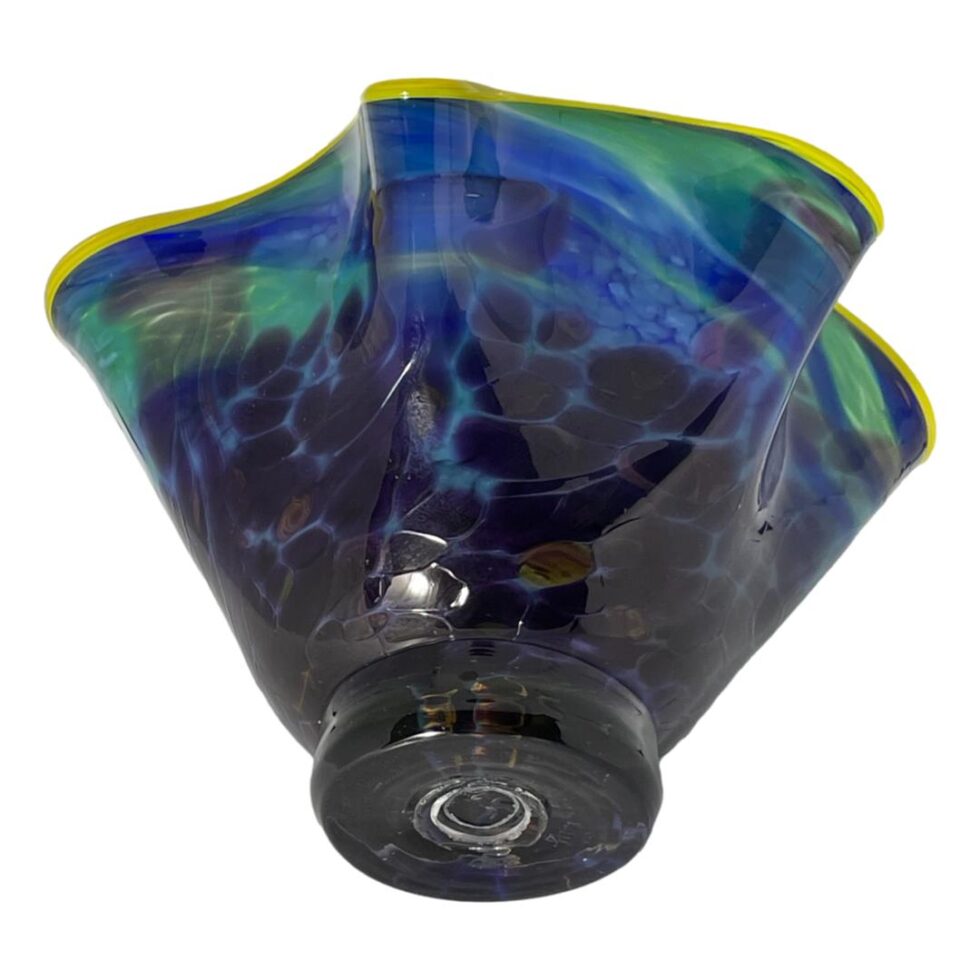 Photo of the Carlyn Ray bowl laid on its side with the base on display. The pontil is visible at the centre showing it is a hand blown piece of glass art. The lower part of the bowl has patches of purple from the outside but appear blue inside.