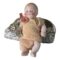 Main photo of miniature German bisque doll displayed leaning against a small rock and forward facing. The doll has painted ginger hair and eyebrows and blue eyes, rosy cheeks and a small red mouth. A fair amount of grubbiness is dotted around its face like its had a really good time playing in the dirt (we've all been there!) The clothes are in quite a poor state. In pale orange, it is like a fine muslin cloth which has clearly not stood the test of time. The pants are literally just hanging on while the top is in slighter better condition. There is a red bow visible to the right shoulder.